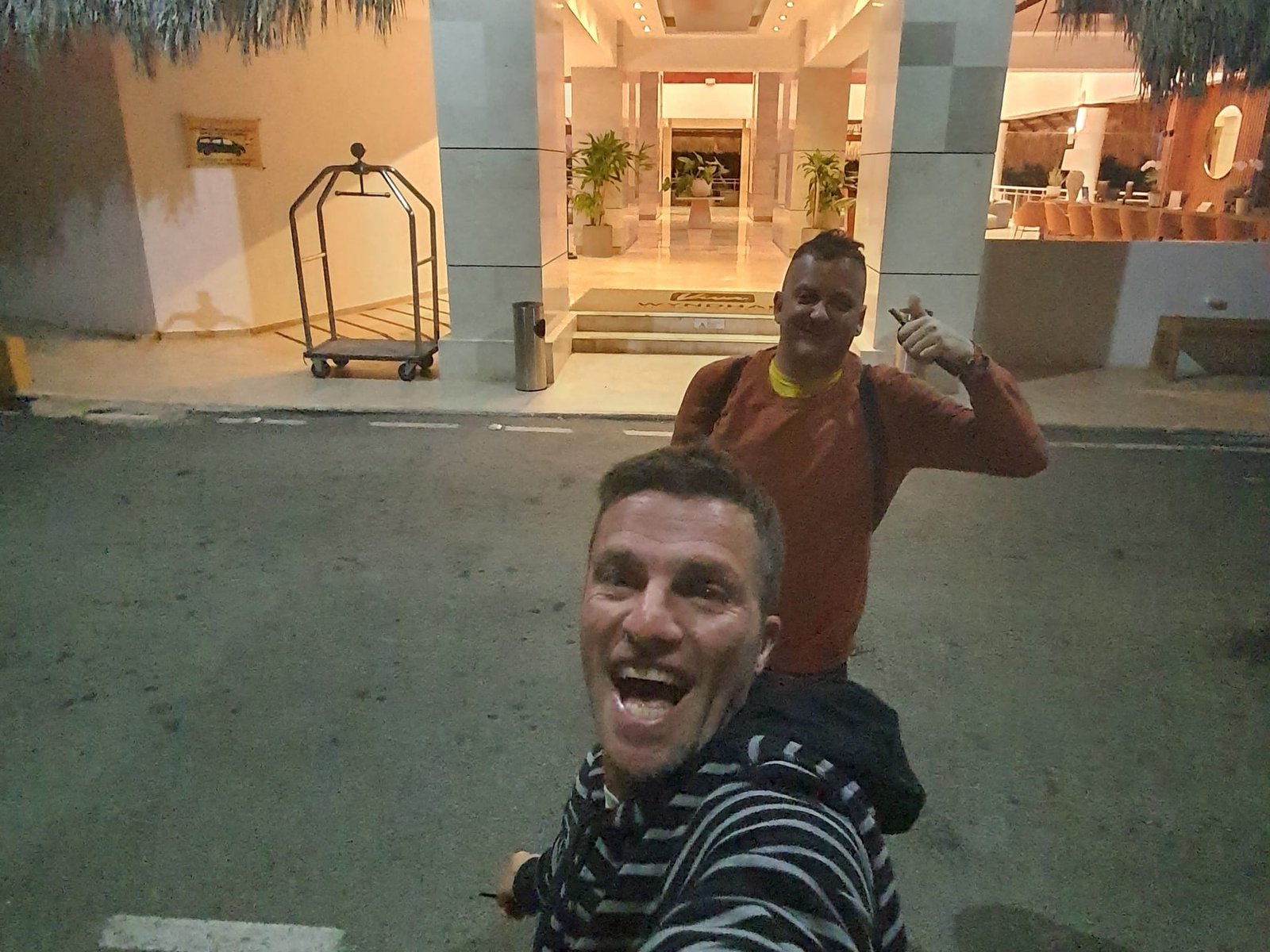 Ale e un amico davanti all’ingresso di un hotel, la sera, con il carrello dei bagagli