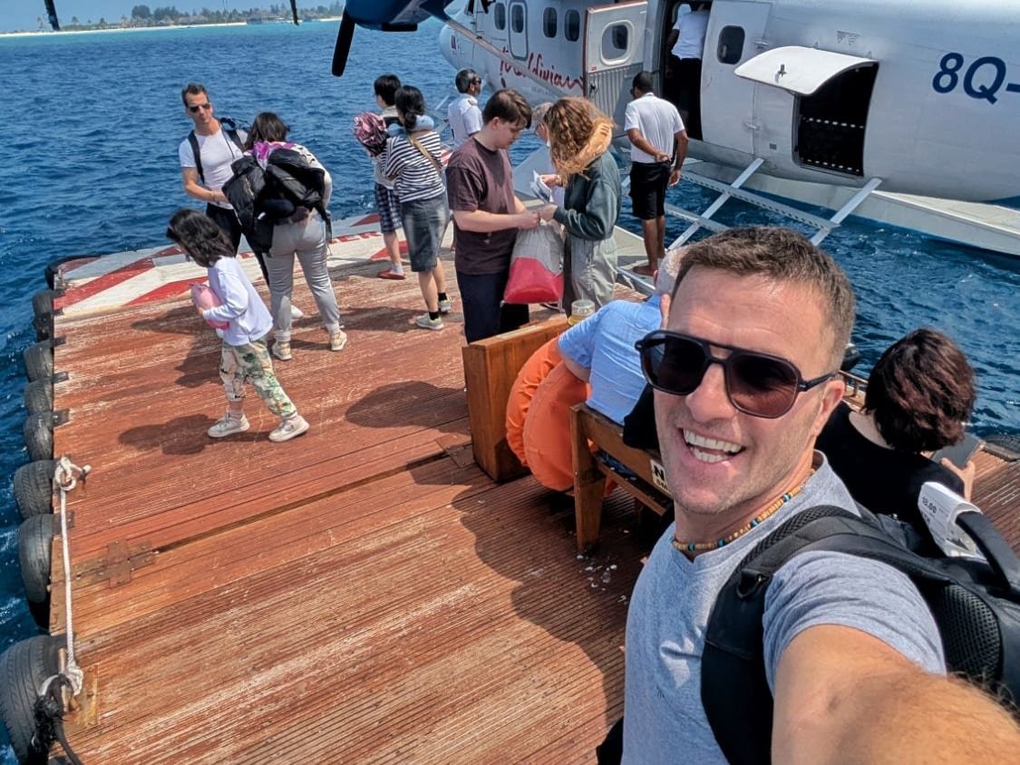Ale con lo zaino in spalla sul pontile, accanto all’idrovolante e agli altri passeggeri con i bagagli