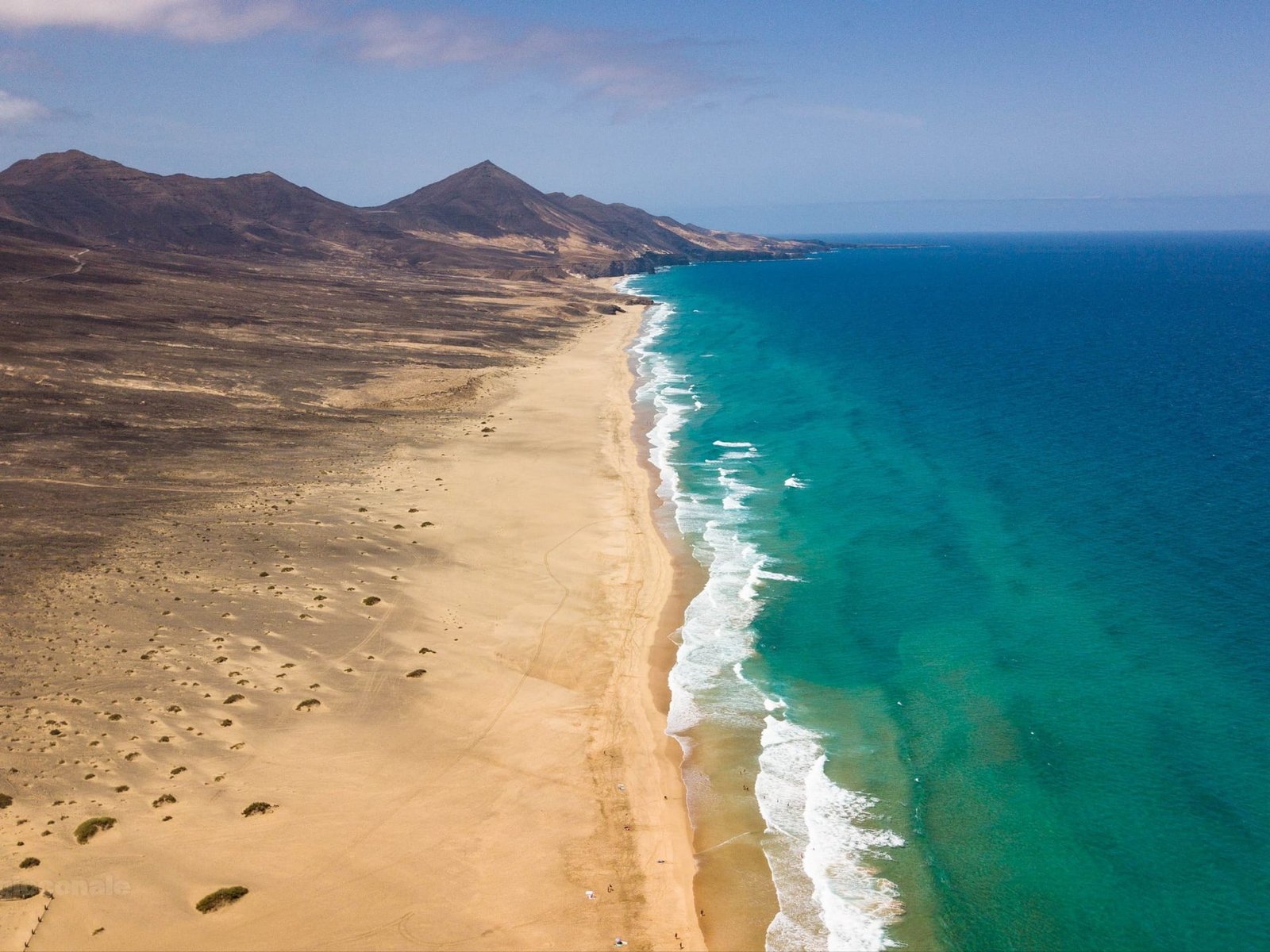 Veduta dal drone di una lunga spiaggia deserta ai piedi delle montagne, a Fuerteventura