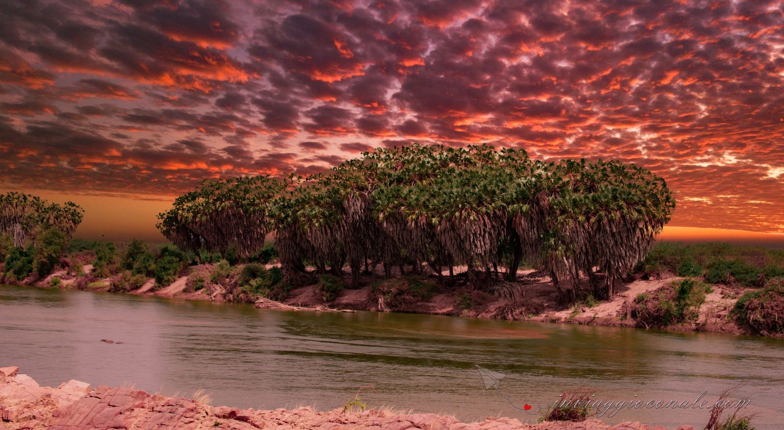 Il fiume tra la vegetazione sotto un cielo rosso fuoco