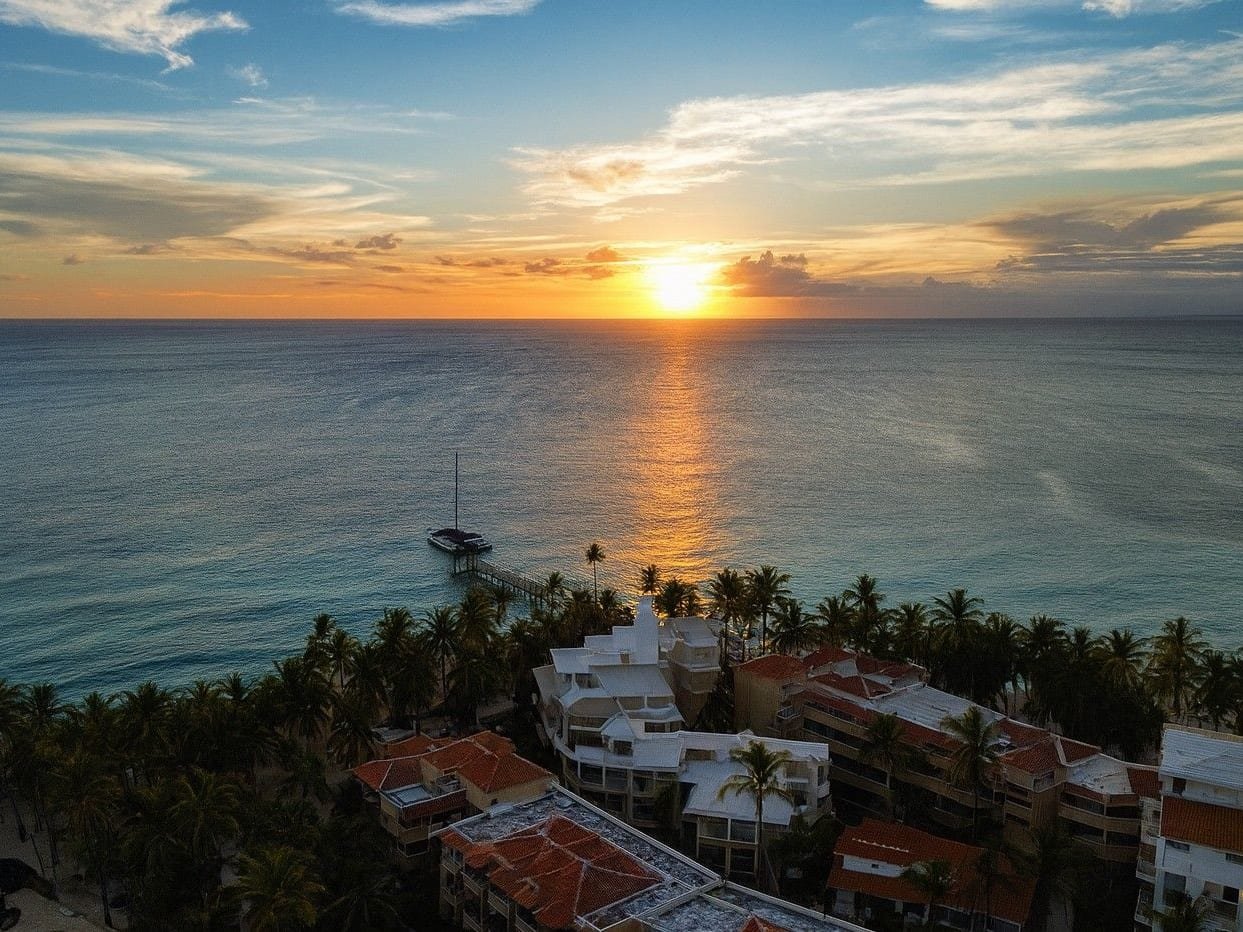 Il tramonto sul mare visto dall’alto, sopra le palme e i tetti rossi di un resort