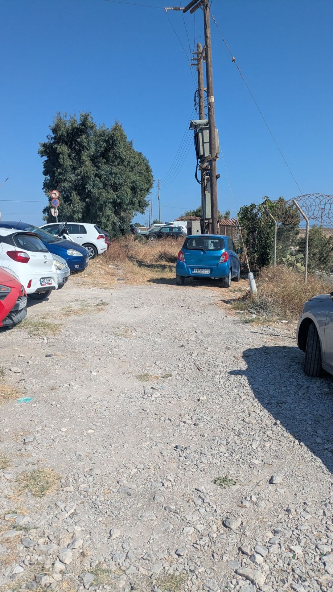 Il parcheggio sterrato dell'aeroporto di Santorini, tra auto in sosta e un palo della luce