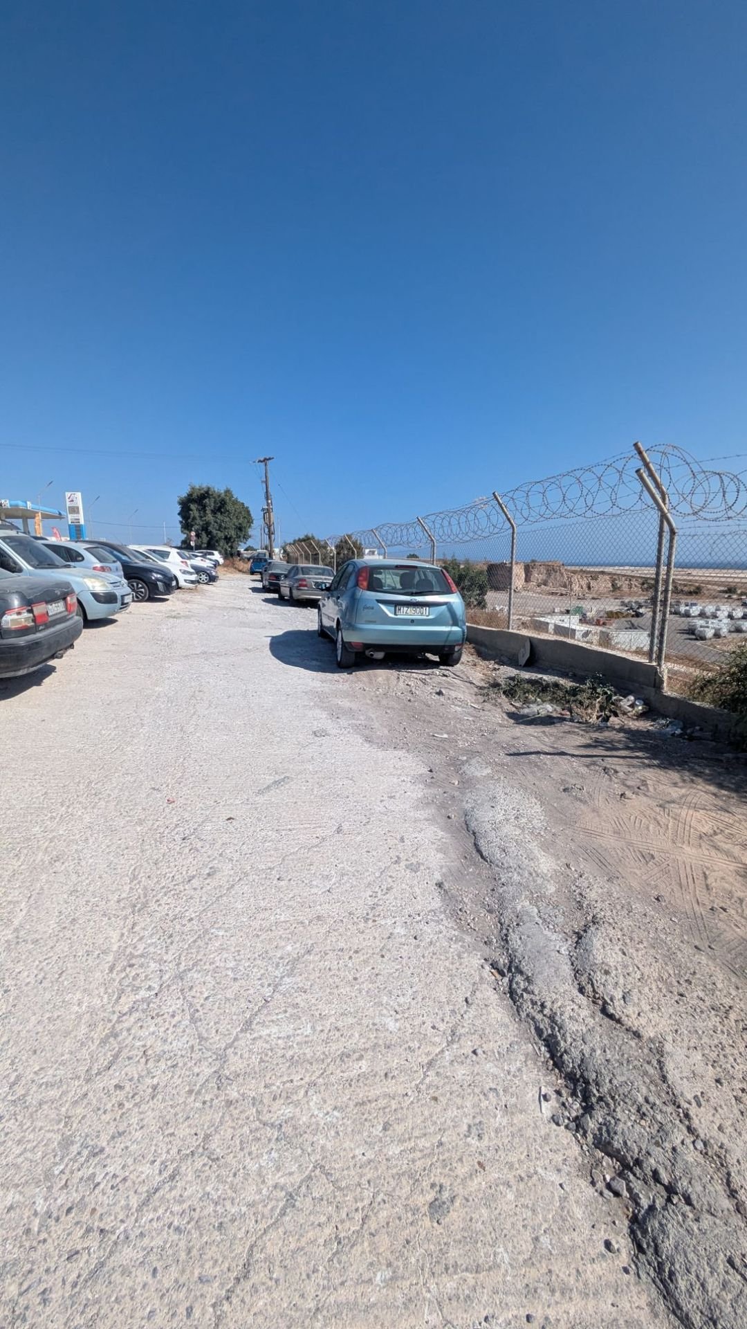 Il parcheggio sterrato vicino all'aeroporto di Santorini, stretto e allungato lungo la recinzione