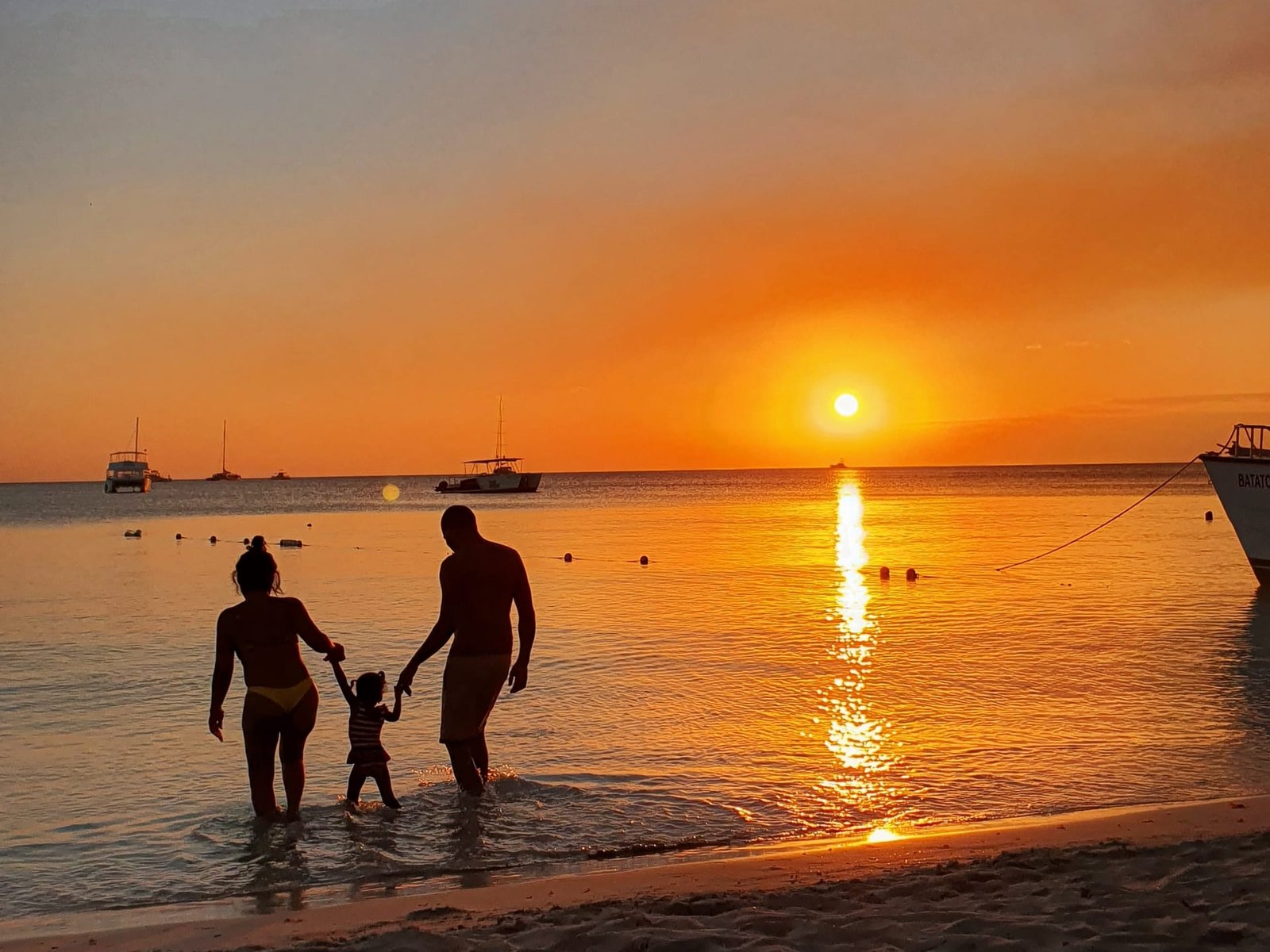Le sagome di una famiglia che cammina in riva al mare al tramonto